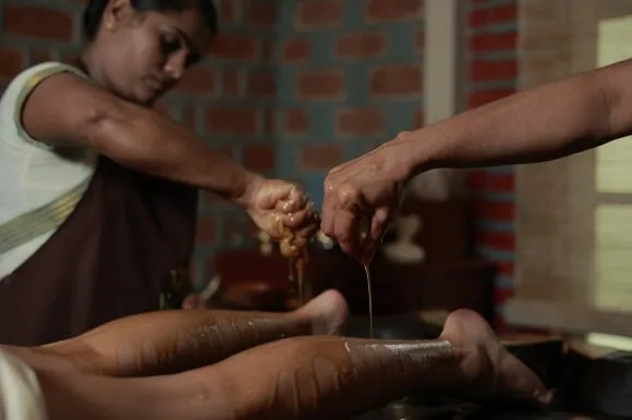 Therapists squeezing warm herbal oil from their hands onto a patient's legs