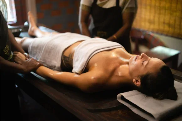 A therapist massages a person's arm as they lie on a wooden treatment table.